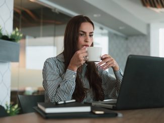 a female drinking coffee and looking down at her laptop