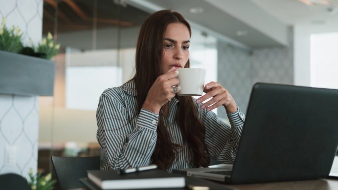 a female drinking coffee and looking down at her laptop